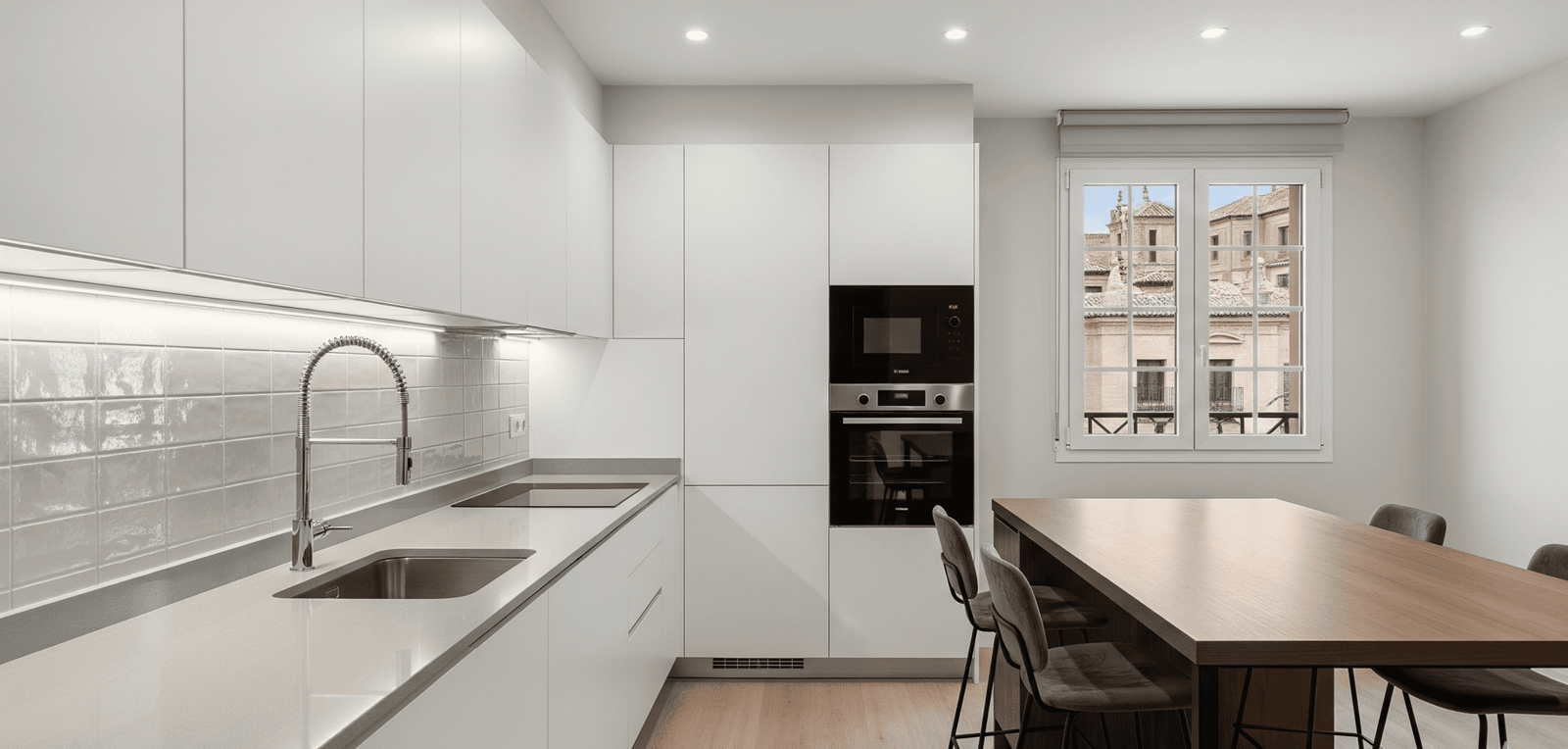 Cocina moderna con office en una reforma de cocina en Alcalá de Henares, destacando el mobiliario blanco sin tiradores y la mesa de madera integrada.