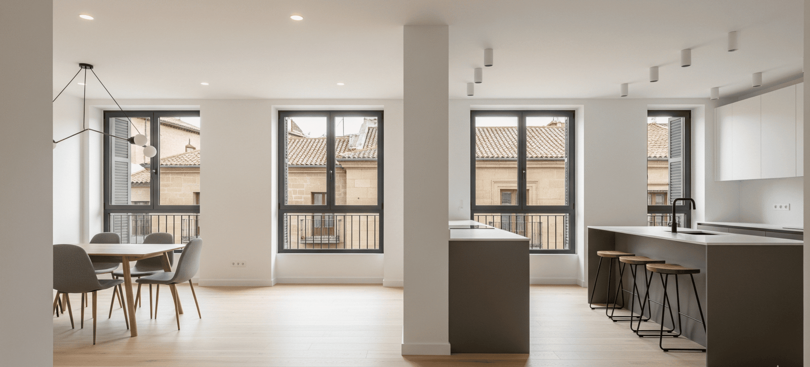 Espacio abierto con cocina y comedor en una reforma integral en Alcalá de Henares, destacando la isla de cocina con taburetes y el suelo de tarima de madera clara.