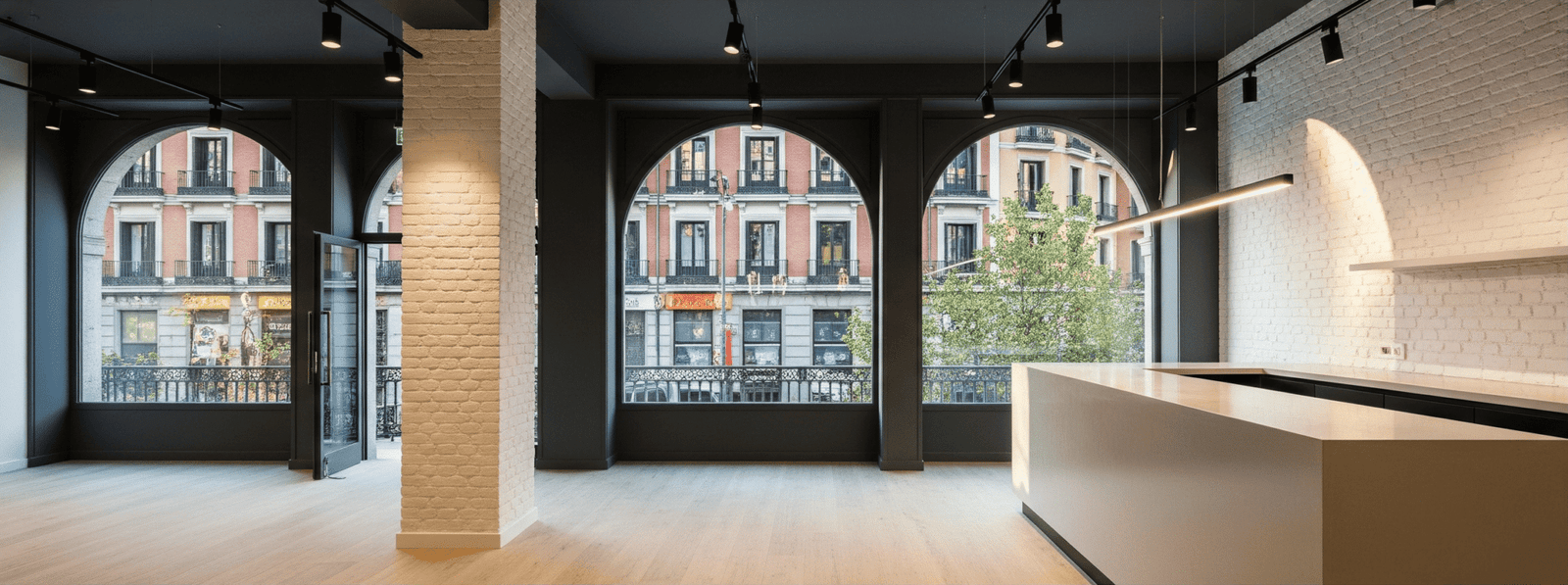 Interior de un local diáfano tras una reforma de local comercial en Madrid, destacando los grandes ventanales en arco y las paredes de ladrillo visto.